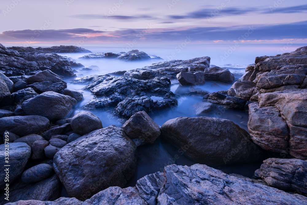 A pre-dawn photograph of misty waves crashing on the rocks by the South Coast in South Africa A pre-dawn photograph of misty waves crashing on the rocks by the South Coast in South Africa