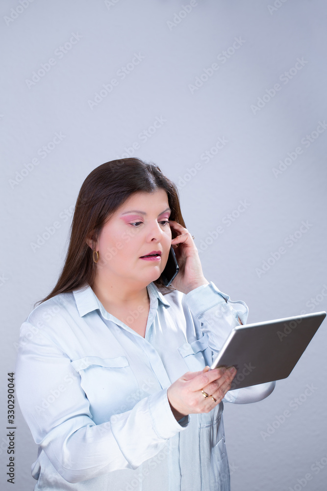 Business Woman Poses for a Studio Portrait. She is speaking on her smartphone and reading information from a tablet. Business Woman Poses for a Studio Portrait. She is speaking on her smartphone and reading information from a tablet.