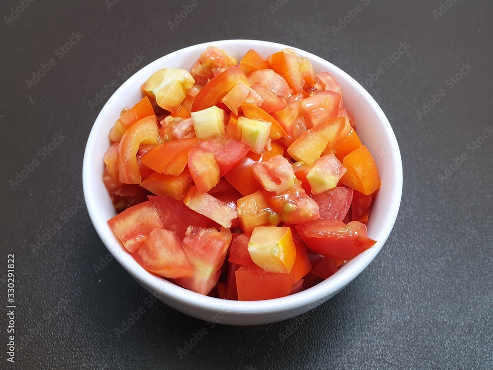 Top view of tomatoes sliced in white bowl isolated on dark background (Solanum lycopersicum var. cerasiforme), Ready to eat or cooking Top view of tomatoes sliced in white bowl isolated on dark background (Solanum lycopersicum var. cerasiforme), Ready to eat or cooking