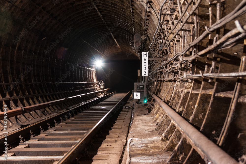 A brightly lit round tunnel with green concrete walls. Railroad tracks laid in concrete turn left. Electric wires are laid along the walls. Electric lighting lamps are lit. A brightly lit round tunnel with green concrete walls. Railroad tracks laid in concrete turn left. Electric wires are laid along the walls. Electric lighting lamps are lit.
