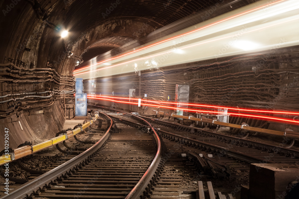 Naklejka premium A passing train the lights of the metro tunnel.At the intersection of two metro lines.Goes into the tunnel.With red lines