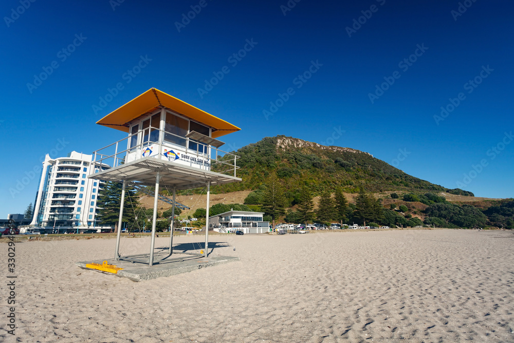Obraz premium MOUNT MAUNGANUI, NEW ZEALAND - MARCH 6, 2020: The Surf Lifesaving tower stands ready on the Mount Main Beach on a beautiful sunny blue sky Autumn day