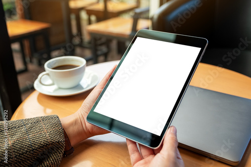 Mockup image of a woman holding black tablet pc with blank white screen with laptop and coffee cup on wooden table