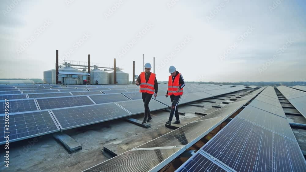 New solar farm under the blue sky. Workers in special outfit walk and talk about sunny cells installation. Modern solar panels produce clean electricity.