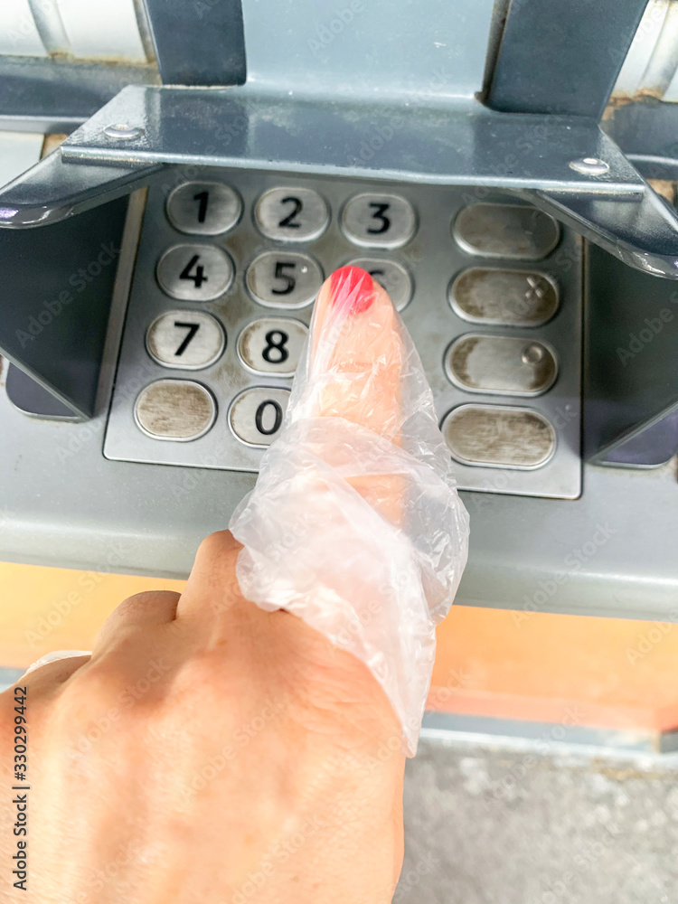 Fototapeta premium Coronavirus and cash. Woman presses a finger on an ATM. Using a plastic bag or gloves on your hand to avoid viruses, germs, bacteria from dirty ATM buttons.
