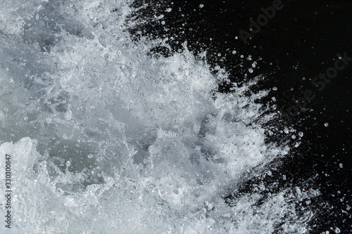 A textured close up macro photograph of water spray and drops against a black background.