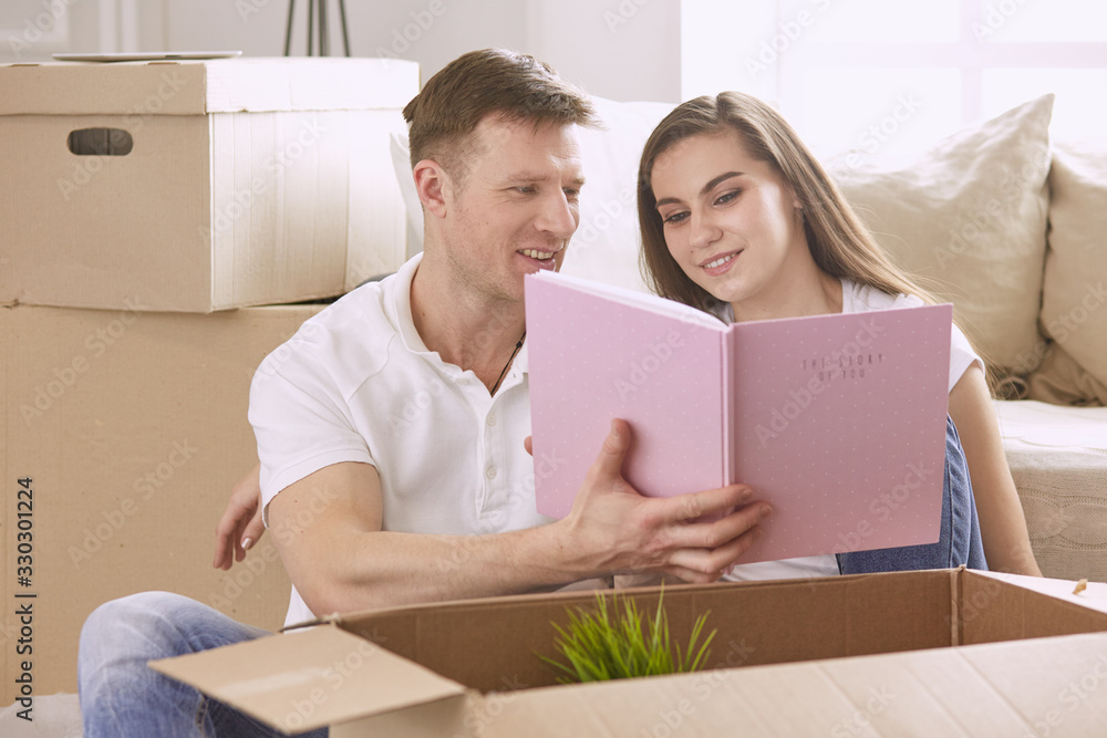 Portrait of happy couple looking at laptop computer together sitting in new house, surrounded with boxes Portrait of happy couple looking at laptop computer together sitting in new house, surrounded with boxes