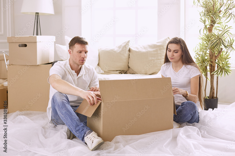Portrait of happy couple looking at laptop computer together sitting in new house, surrounded with boxes Portrait of happy couple looking at laptop computer together sitting in new house, surrounded with boxes