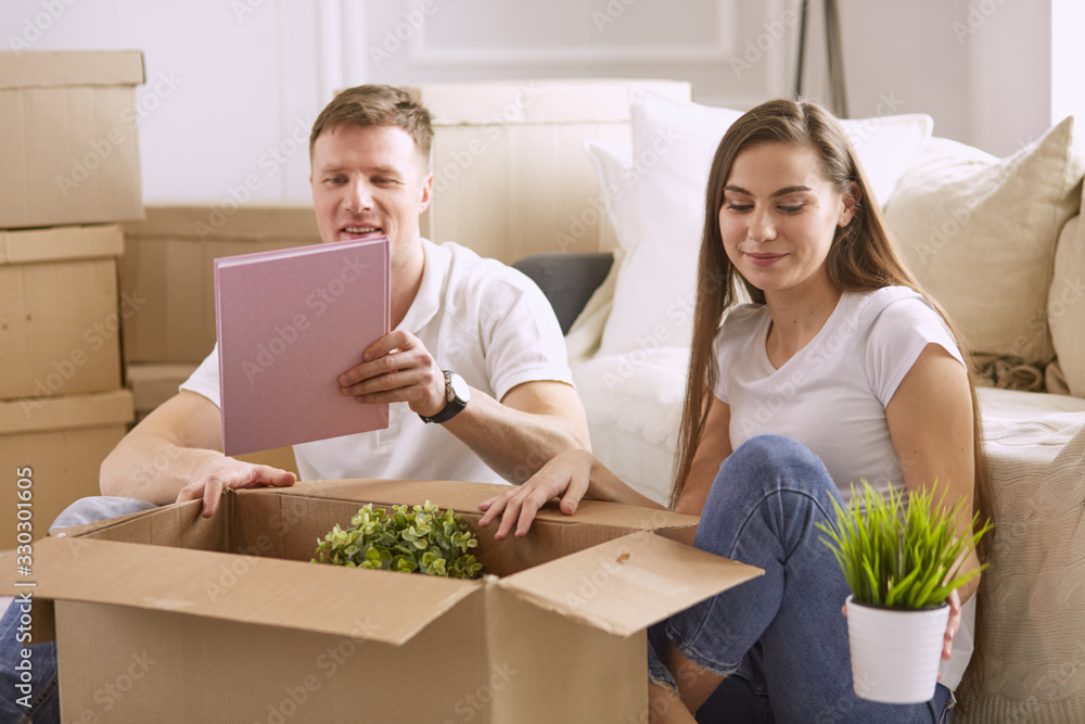 Portrait of happy couple looking at laptop computer together sitting in new house, surrounded with boxes Portrait of happy couple looking at laptop computer together sitting in new house, surrounded with boxes