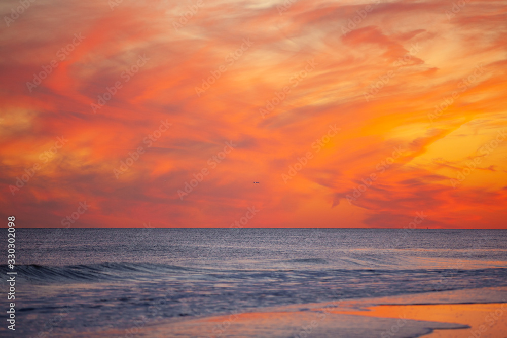 Commercial airplane approaching its destination over a beach during a vibrant pink and orange sunset. 