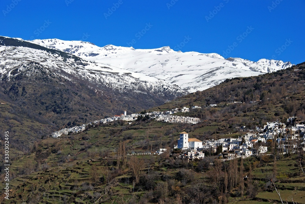View of the town of Bubion with Capileira town to the rear viewed against a backdrop of the snow capped mountains of the Sierra Nevada, Bubion, Spain.
