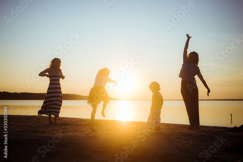 Silhouettes of children and their mothers jumping and having fun on the beach in sunset light. Good mood and pastime among the younger and older generation.