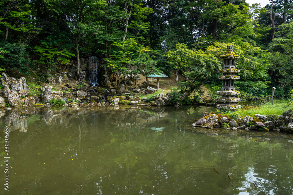 Small waterfall and stone lantern on the near the Hisagoike pond at Kenrokuen garden, Kanazawa, Japan Small waterfall and stone lantern on the near the Hisagoike pond at Kenrokuen garden, Kanazawa, Japan