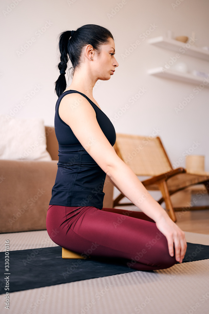 Sporty beautiful young woman practicing yoga, sitting on wooden block in seiza, vajrasana, thunderbolt or diamond asana for meditation, breath work Sporty beautiful young woman practicing yoga, sitting on wooden block in seiza, vajrasana, thunderbolt or diamond asana for meditation, breath work