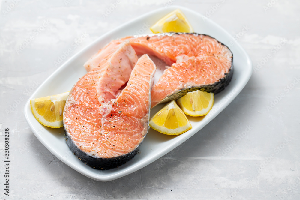 raw salmon with lemon on white dish on ceramic background