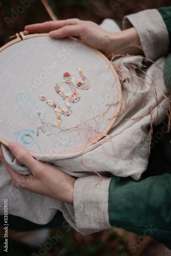 Konstfotografi Hands of girl / woman / female in boho linen dress hold sewing stitching pattern in embroidery frame on the background of park