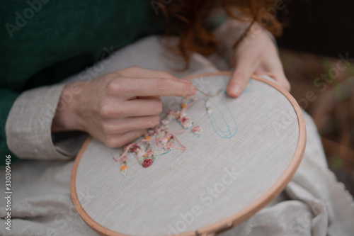 Photography Hands of girl / woman / female in boho linen dress hold sewing stitching pattern in embroidery frame on the background of park