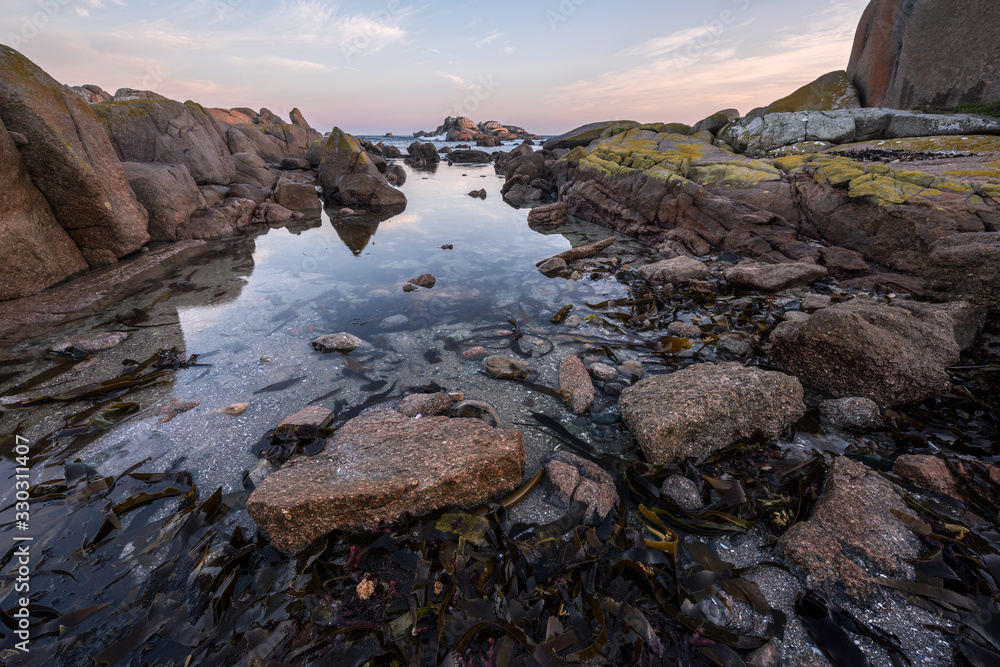 Fototapeta premium A beautiful early morning seascape, with a golden cloudy sky and rocks and reflections in the foreground, taken at Paternoster, South Africa.