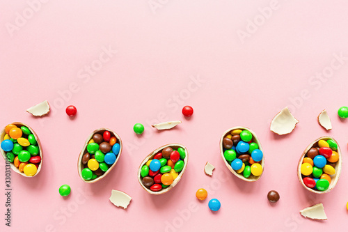 Chocolate Easter eggs and colorful candies on pastel pink paper background. flat lay, top view, overhead, copy space, template, mockup