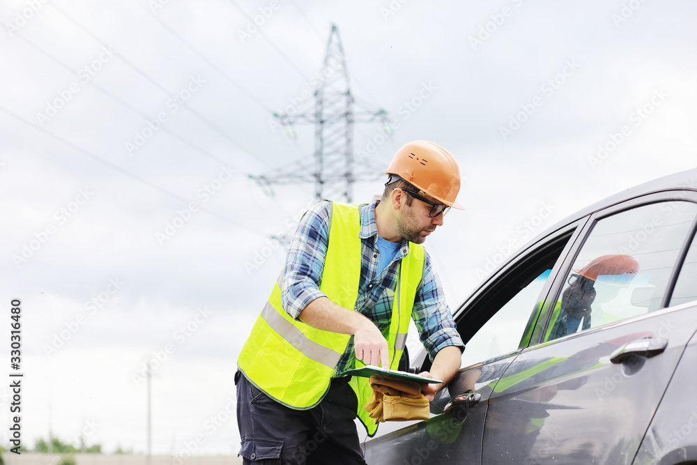 A man in a helmet and uniform, an electrician in the field. Professional electrician engineer inspects power lines during work.