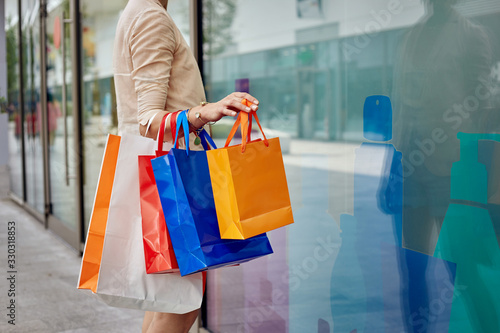 Young girl in a beige blouse and holding multi-colored fashionable shopping bags.