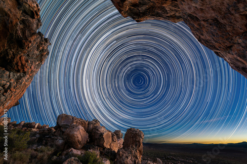 A beautiful night sky photograph with circular star trails framed by dramatic rocks in the foreground, taken in the Cederberg mountains in the Western Cape, South Africa. photo