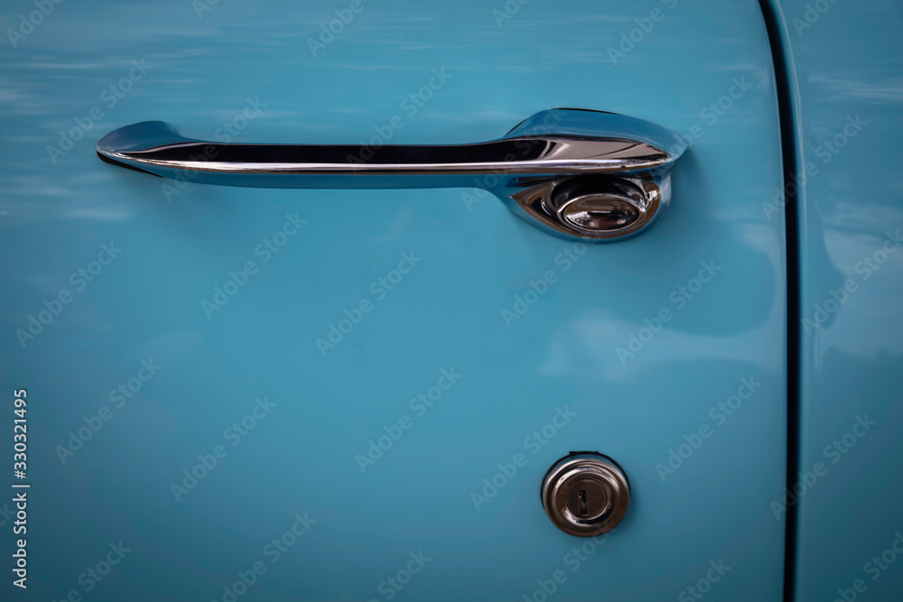 Chrome door handle to a classic 1950s blue automobile