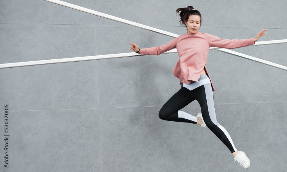 An athletic young woman is jumping, doing acrobatics, ballet, is actively involved in sports, against a concrete wall.