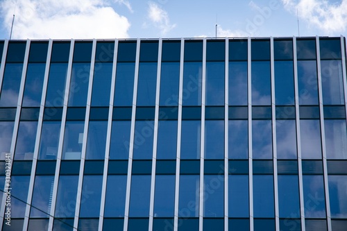 Modern curtain wall made of glass and steel. Blue sky and clouds reflected in windows of modern office building. 