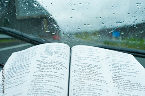 Holy Bible opened inside the car in Psalm 91, on a day of storm and heavy rain. Windshield with raindrops. Background with Tōmei Expressway (Tōmei Kōsoku Dōro), Japan. photo