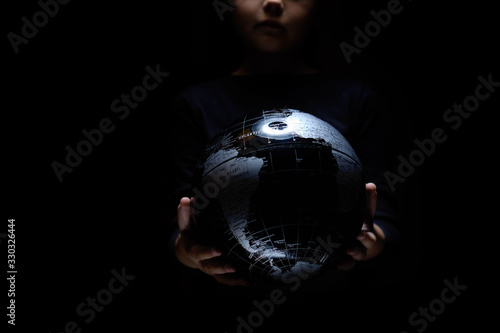 Hands of little girl hold globe sphere map isolated on black background. COVID-19 pandemic infection disease. Environmental pollution, ecological disaster our kids and future planet concept BW image