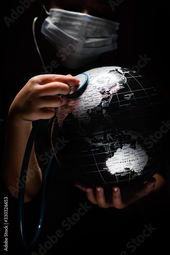 Kid hold globe put stethoscope on sphere, face covered in mask on black background. Ecological problems disasters. COVID-19 pandemic infection disease concept image