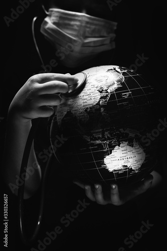 Kid hold globe put stethoscope on sphere, face covered in mask on black background. Ecological problems disasters. COVID-19 pandemic infection disease concept black and white image