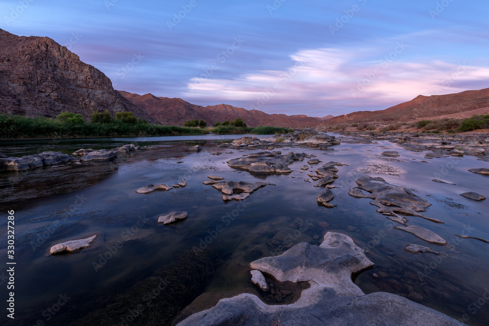 A beautiful long exposure landscape taken after sunset with mountains and the Orange River, with dramatic moving clouds reflecting in the water’s surface, taken in the Richtersveld South Africa.