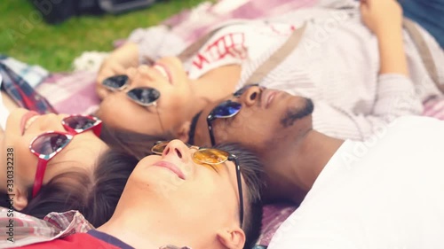 Young guys and girls of different races lie on grass head to head. Top view two girls and two guys are resting lying on the grass. Group of young students lies on grass in the break between classes. photo