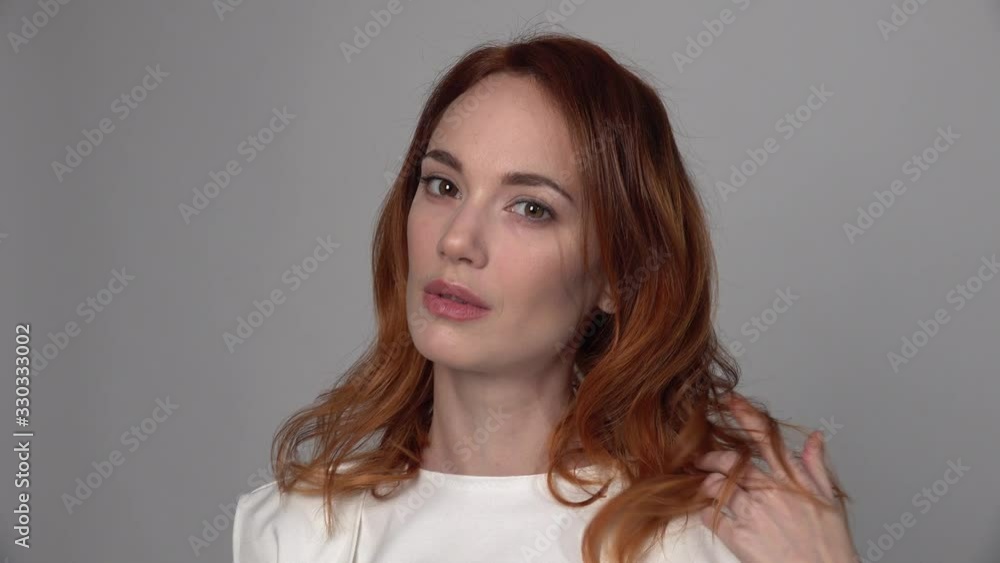 Nice young redhead woman posing for camera y and waves her hair on neutral background Nice young redhead woman posing for camera y and waves her hair on neutral background