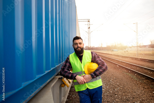 Photos Portrait of railway worker standing by the train trailer with shipping containers at station