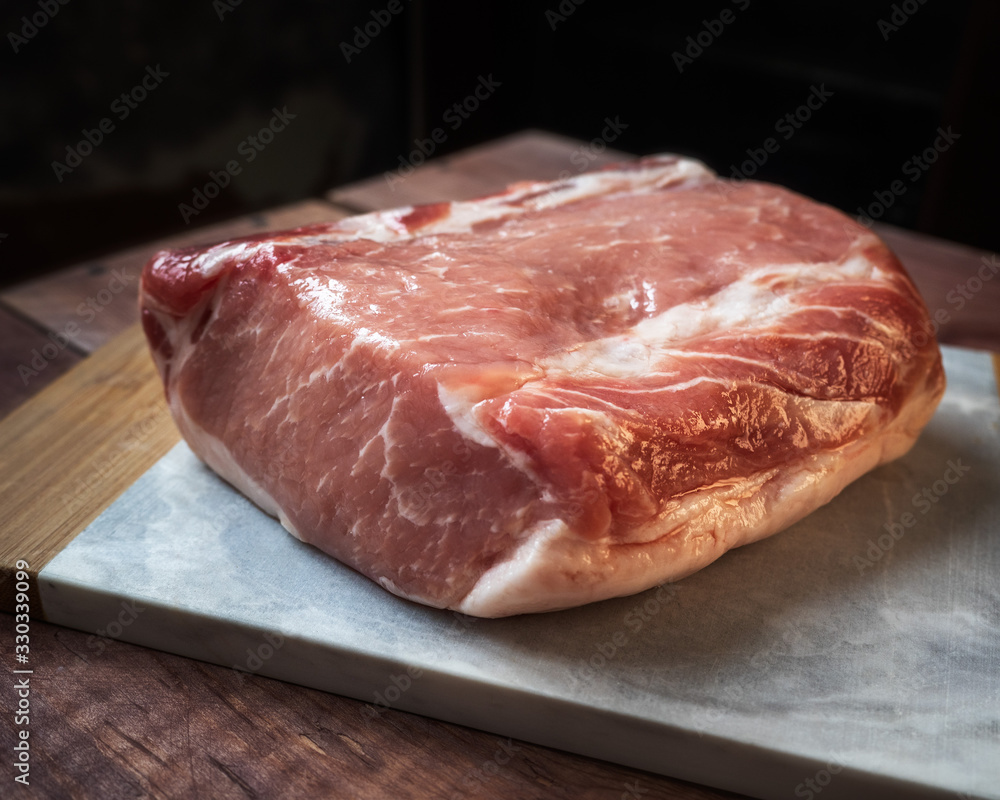 Raw piece of pork lies on the kitchen board, lying on a wooden table