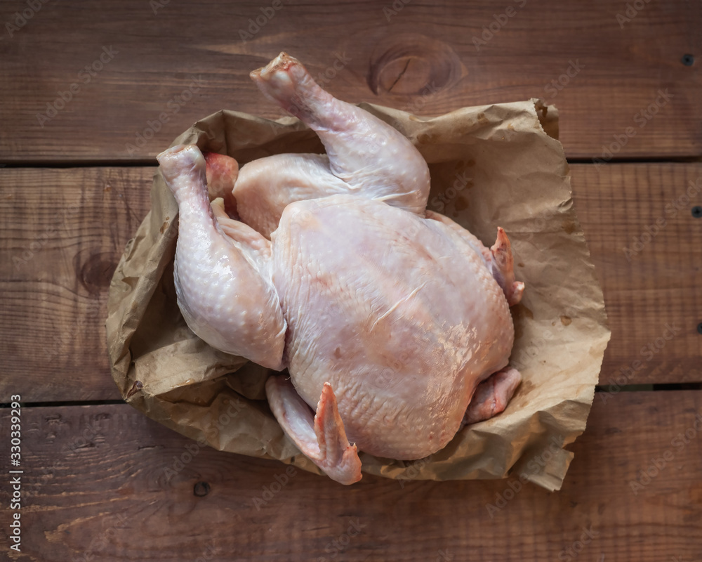 Plucked chicken carcass lies on a paper bag on a wooden table, closeup