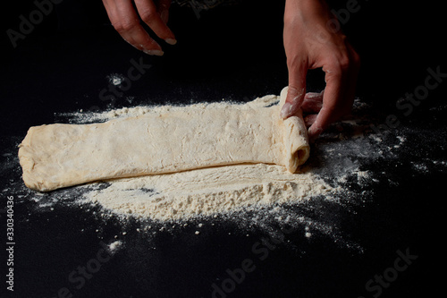 Professional Female cook sprinkles dough with flour, prepared for baked bread
