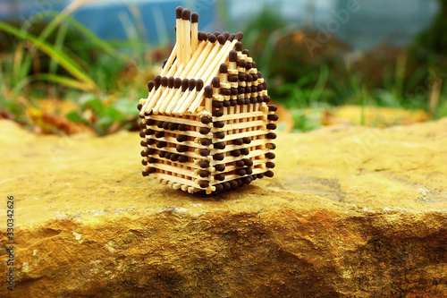 Matchstick mini house stands on a golden rocky stone