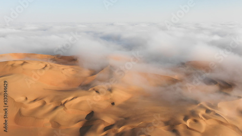 Aerial view of a massive sand dune surrounded by winter morning fog cloud in Empty Quarter. Liwa desert, Abu Dhabi, United Arab Emirates.