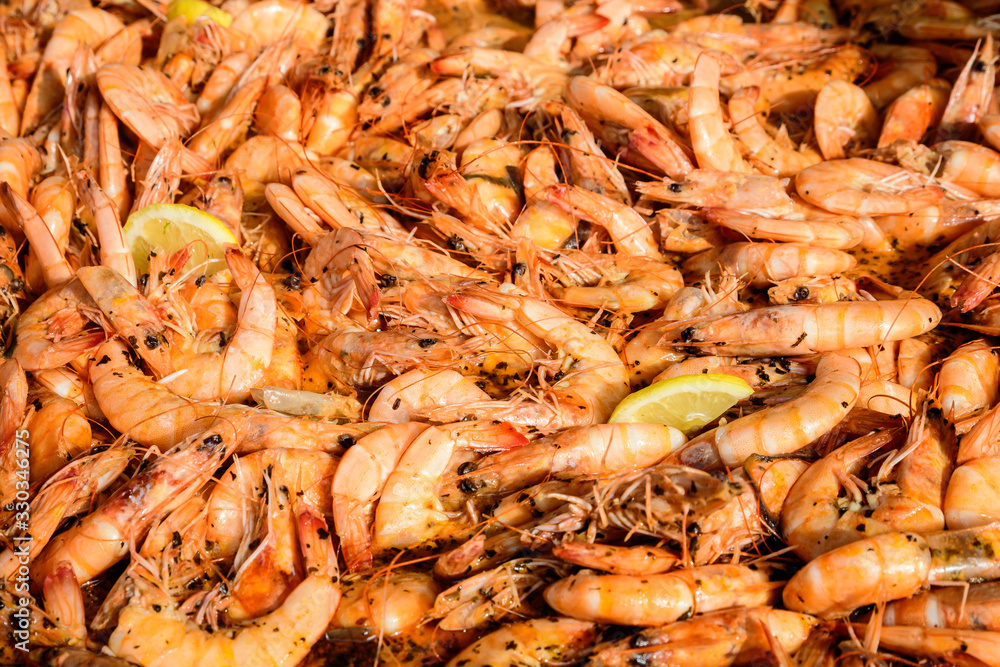 Close up of large portion of cooked shrimps with tomato sauce and yellow lemons in a large pan at a street food festival, ready to eat healthy seafood, beautiful orange monochrome outdoor background Close up of large portion of cooked shrimps with tomato sauce and yellow lemons in a large pan at a street food festival, ready to eat healthy seafood, beautiful orange monochrome outdoor background