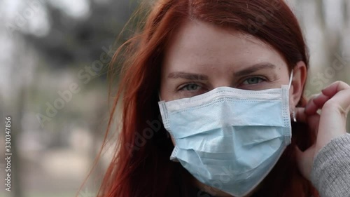 Coronavirus. Portrait of a young tourist woman in a medical mask feeling sick looks at the camera in the park. Blurred background. photo