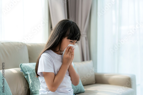 Asian child or kid girl sick and sad with sneezing on nose and cold cough on tissue paper because influenza and weak or virus bacteria from dust weather or smoke and kindergarten school for medical..