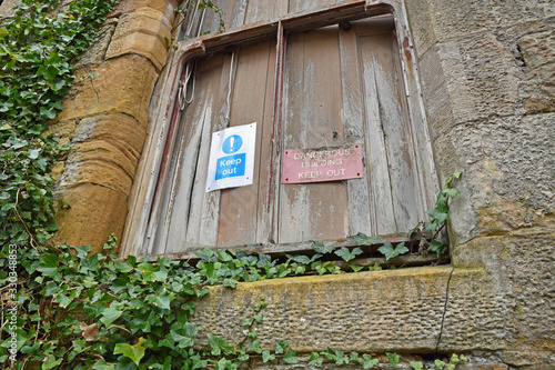 Murais de parede Keep out dangerous building signs on boarded up window with climbing ivy surrounding