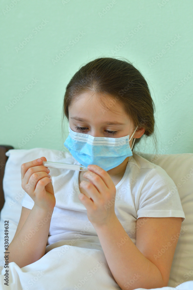 girl looks at a high-temperature thermometer.Quarantine.Blue infection preventive face mask . I virus infection in Corona virus crisis 2020. Take care kids from infection.