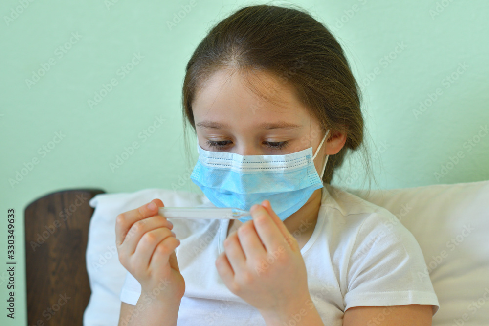 girl looks at a high-temperature thermometer.Quarantine.Blue infection preventive face mask . I virus infection in Corona virus crisis 2020. Take care kids from infection. girl looks at a high-temperature thermometer.Quarantine.Blue infection preventive face mask . I virus infection in Corona virus crisis 2020. Take care kids from infection.