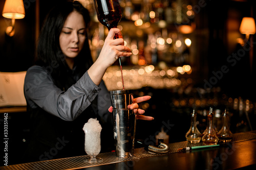 Woman bartender pours alcoholic drink from bottle into shaker.