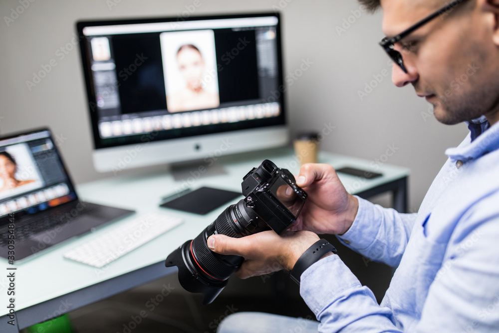 Handsome photographer holding his camera smiling at camera in creative office ready for editing photo Handsome photographer holding his camera smiling at camera in creative office ready for editing photo
